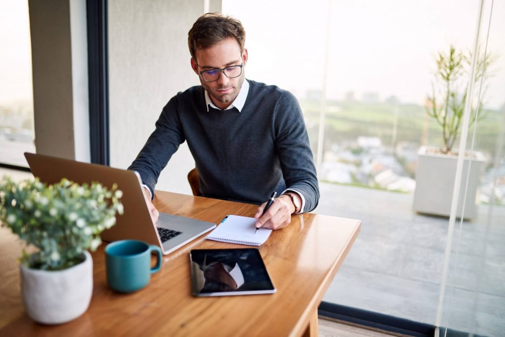 Man On Laptop Writing Notes