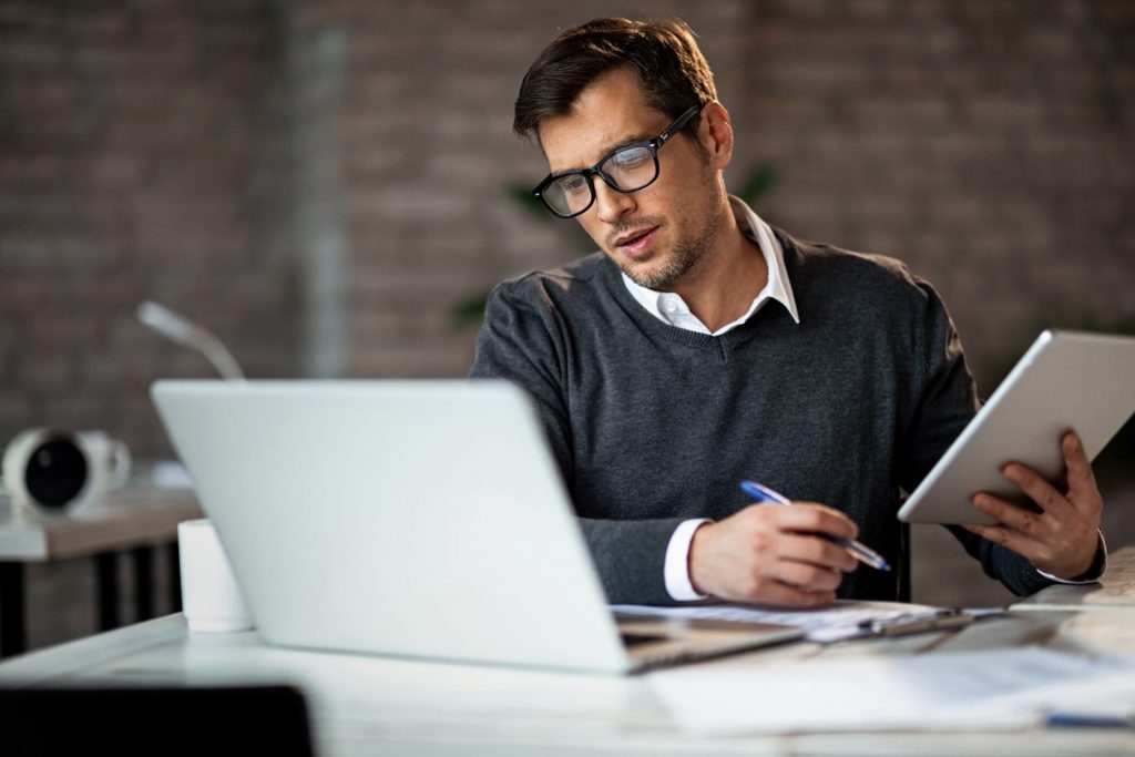 Man On Laptop And Taking Notes