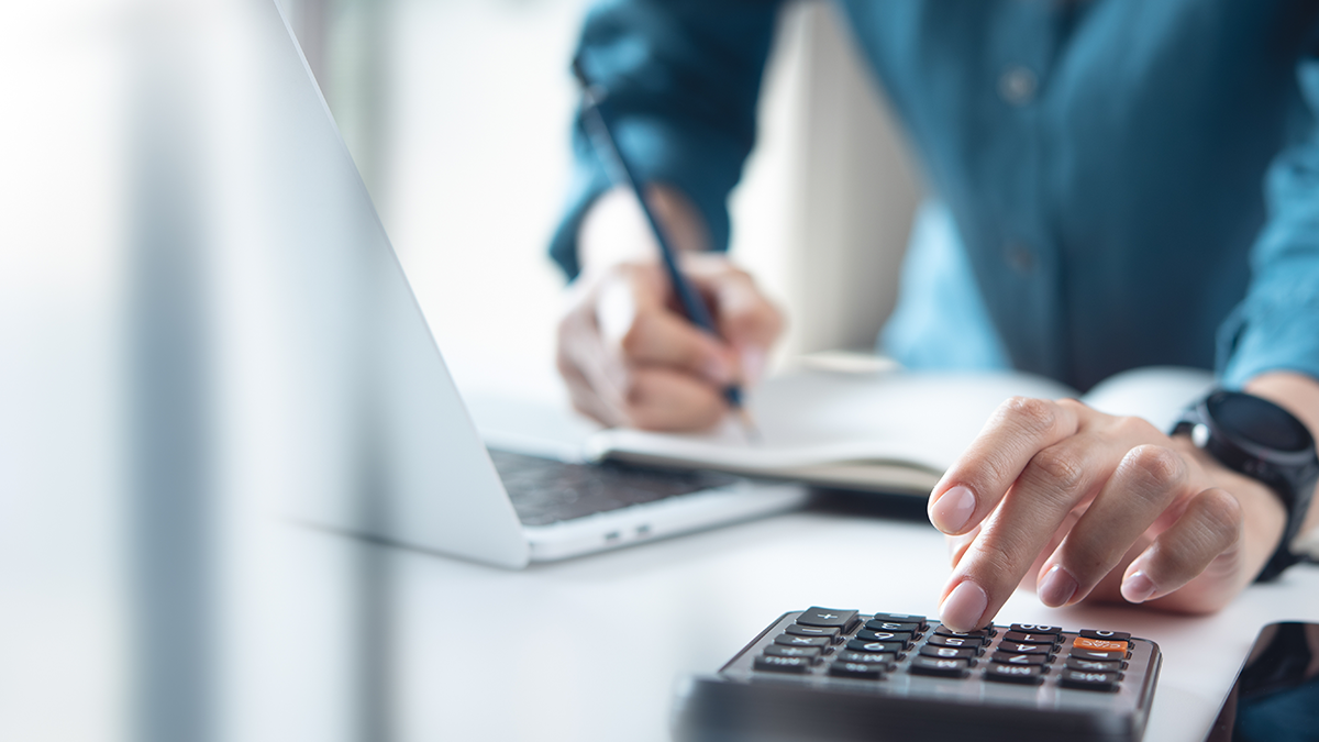 A man typing in a calculator whilst writing down in his note pad
